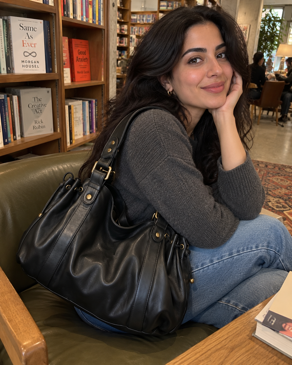 The Valen Hobo in Classic Black styled with a dark sweater and blue jeans in a bookstore.