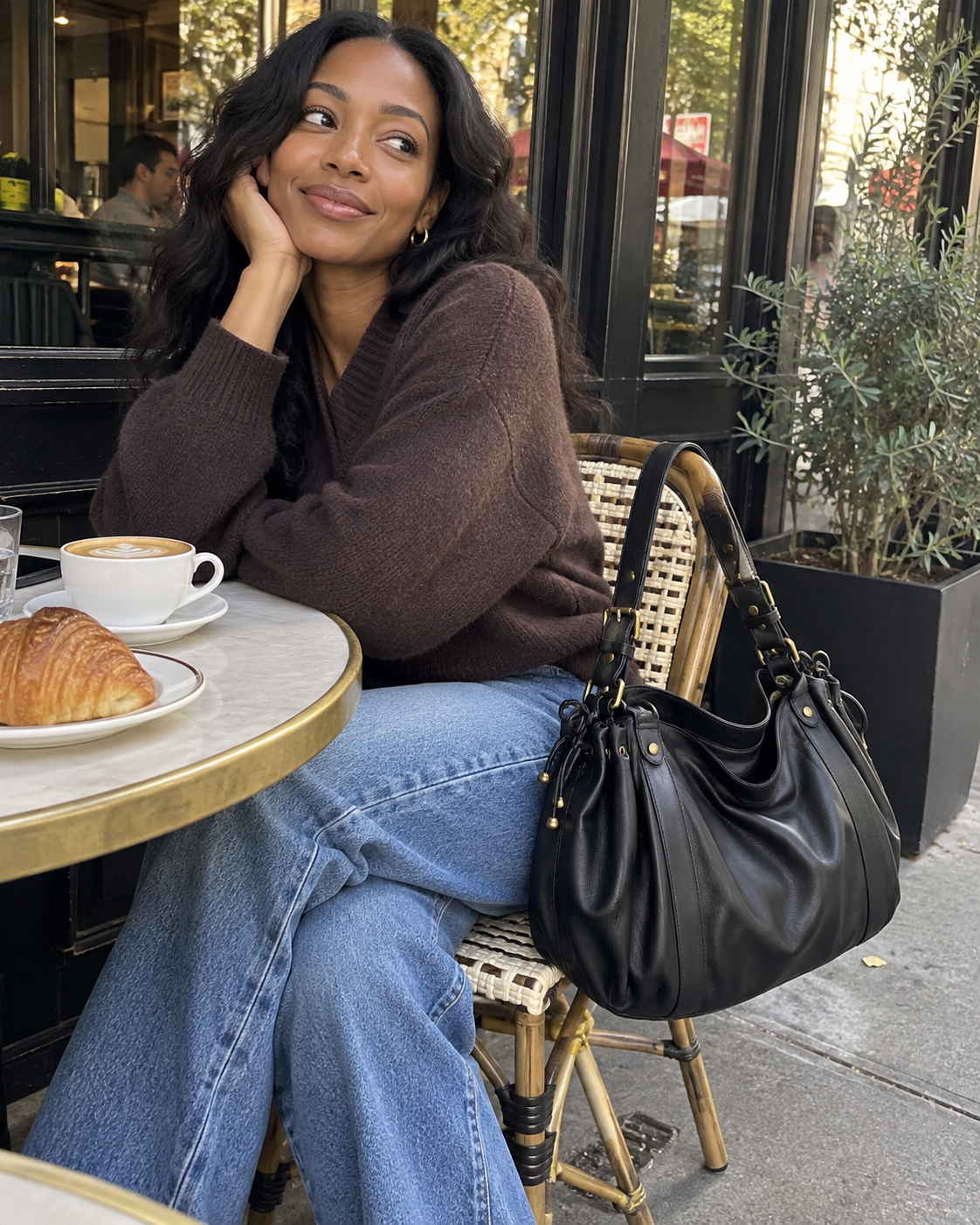 The Valen Hobo in Classic Black styled with a brown sweater and blue jeans at an outdoor café.